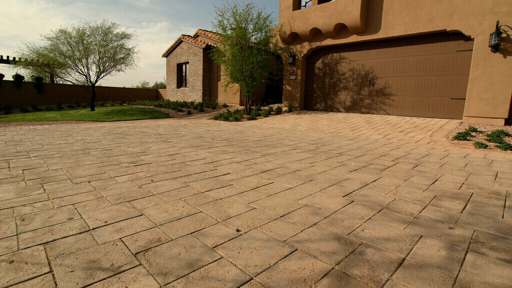 Warm tan block paving across a driveway, laid in a running-bond pattern towards a timber garage door
